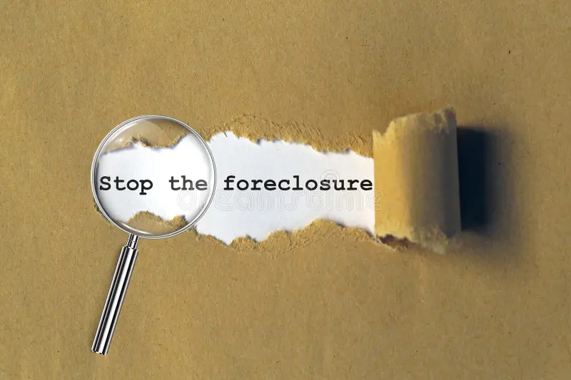 Torn brown paper revealing the words stop the foreclosure under a magnifying glass